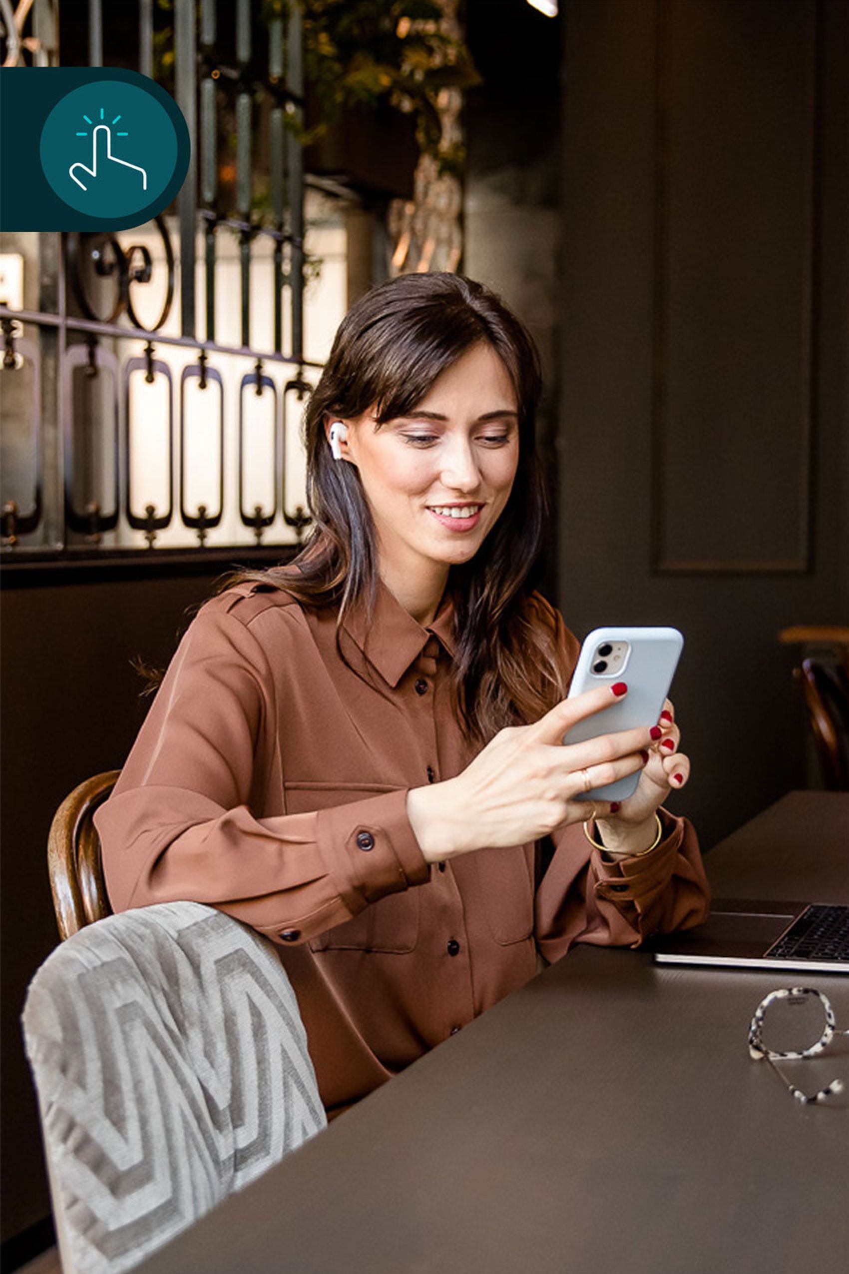 Junge Frau sitzt entspannt in stilvollem Ambiente, schaut lächelnd auf ihr Smartphone, wirkt zufrieden und verbunden.