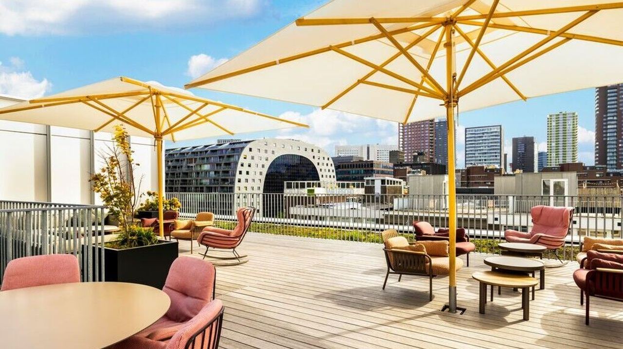 Dachterrasse mit Sitzgruppen und großen Sonnenschirmen, Blick auf die urbane Skyline einer Stadt mit markanten Gebäuden.