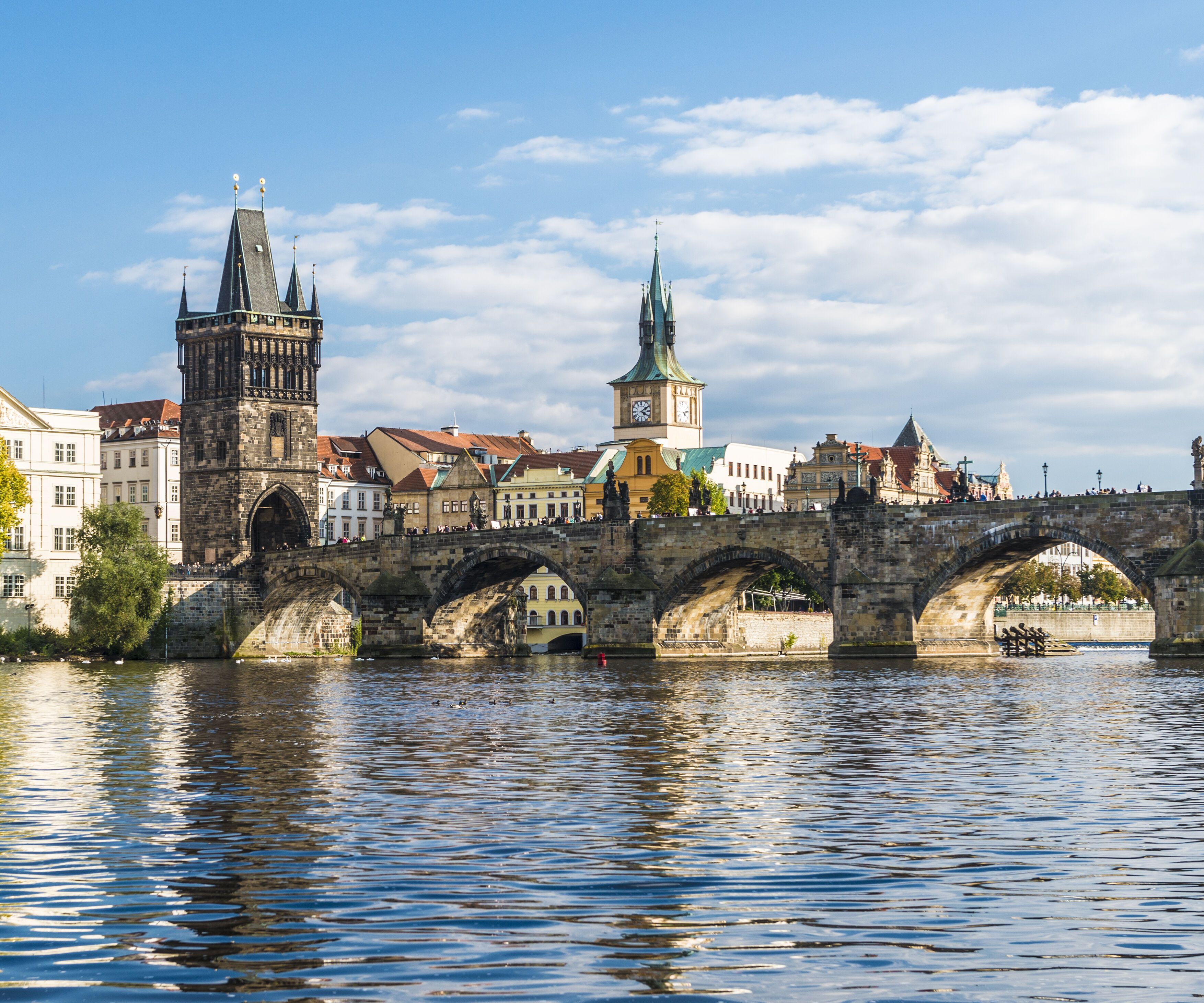 Panoramablick auf die historische Karlsbrücke und barocke Gebäude in Prag, reflektiert im ruhigen Fluss bei klarem Himmel.