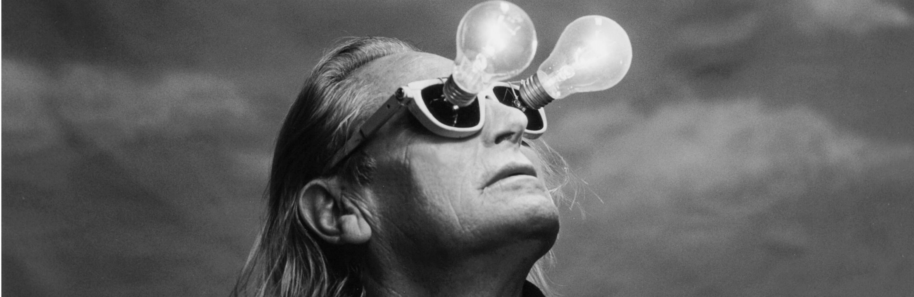 Ein Mann blickt mit ungewöhnlicher Brille, die Glühbirnen statt Gläser hat, nach oben – Symbol für kreative Ideen und neue Perspektiven.