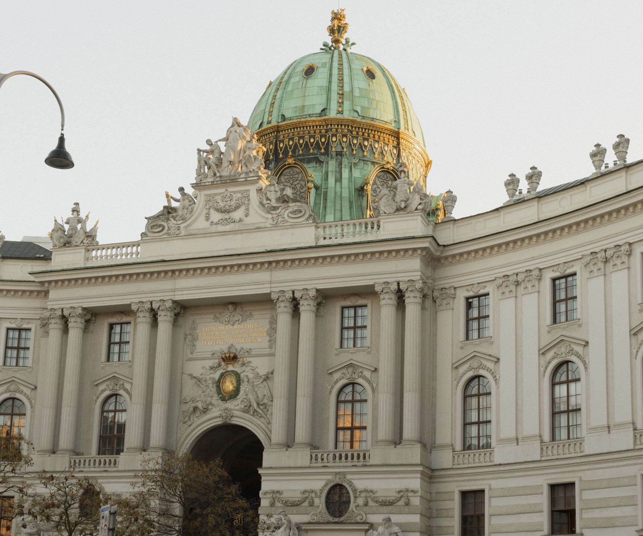 Barockes Gebäude mit großer grüner Kuppel und verzierten Fassaden, Menschen und Autos vor dem Haupteingang.