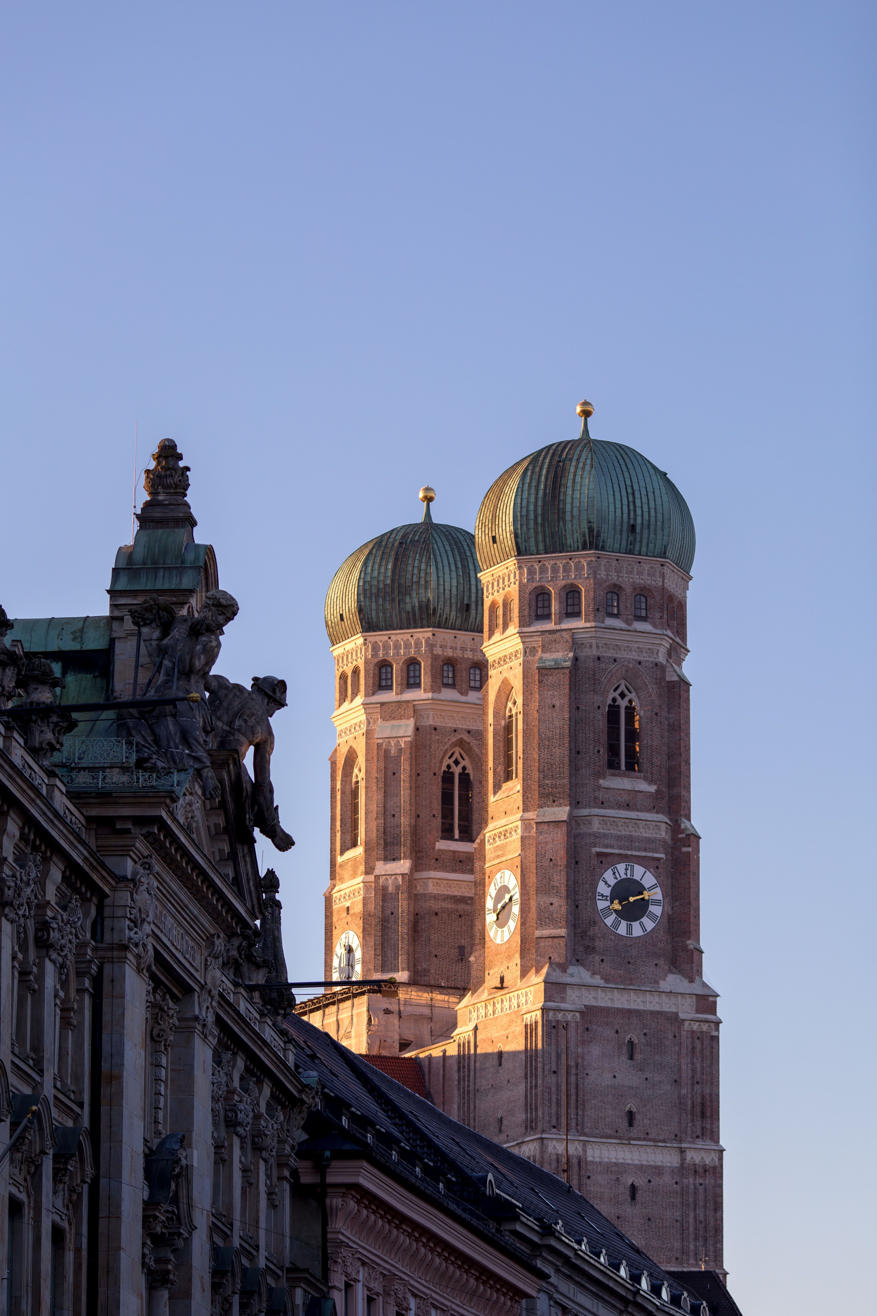 Die beiden markanten Zwiebeltürme der Frauenkirche in München leuchten im warmen Abendlicht vor klarem Himmel.