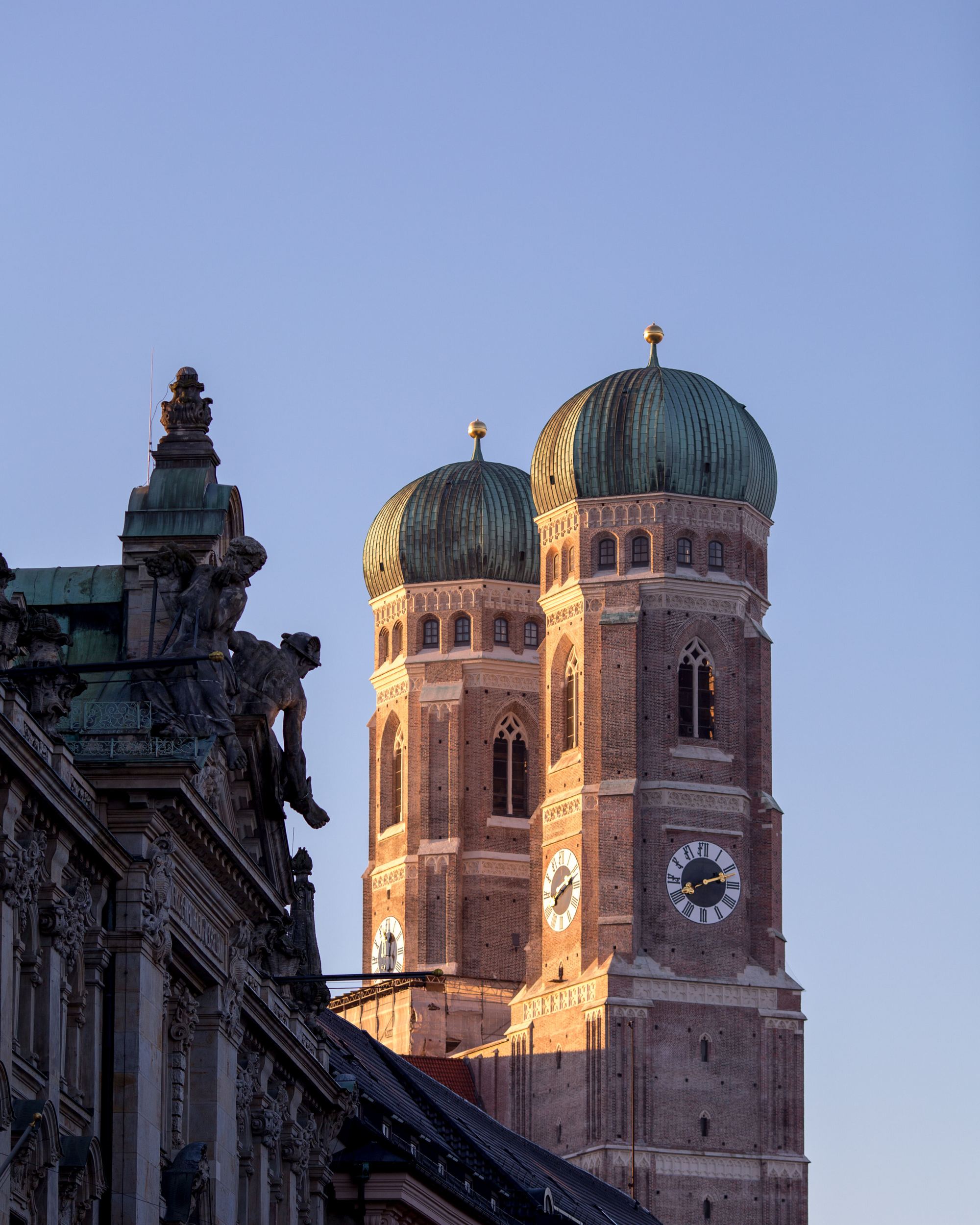 Die beiden markanten Zwiebeltürme der Frauenkirche in München leuchten im warmen Abendlicht vor klarem Himmel.