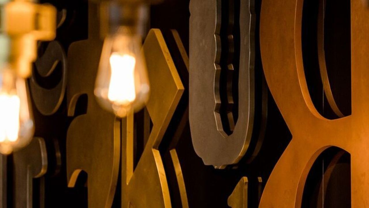 Detailaufnahme von warm beleuchteten, dekorativen Metallzahlen und Buchstaben an einer Wand