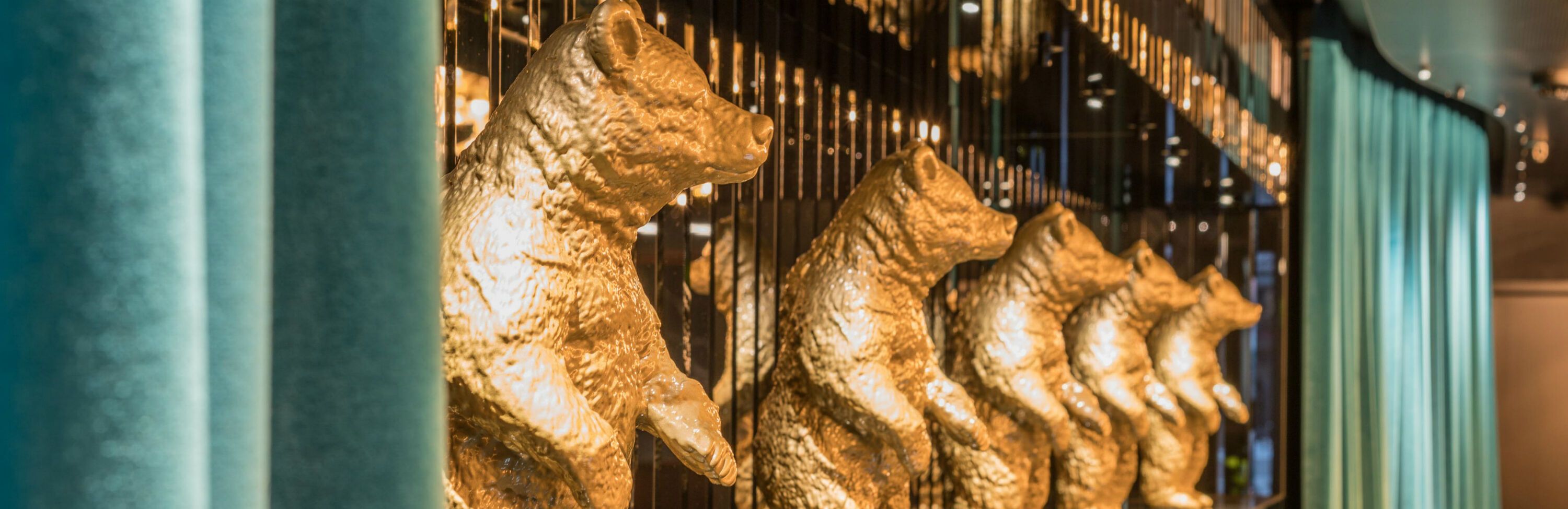 Reihe goldener Bärenfiguren an einer stilvollen, modernen Wanddekoration, die Eleganz und Raffinesse im Motel One vermittelt.