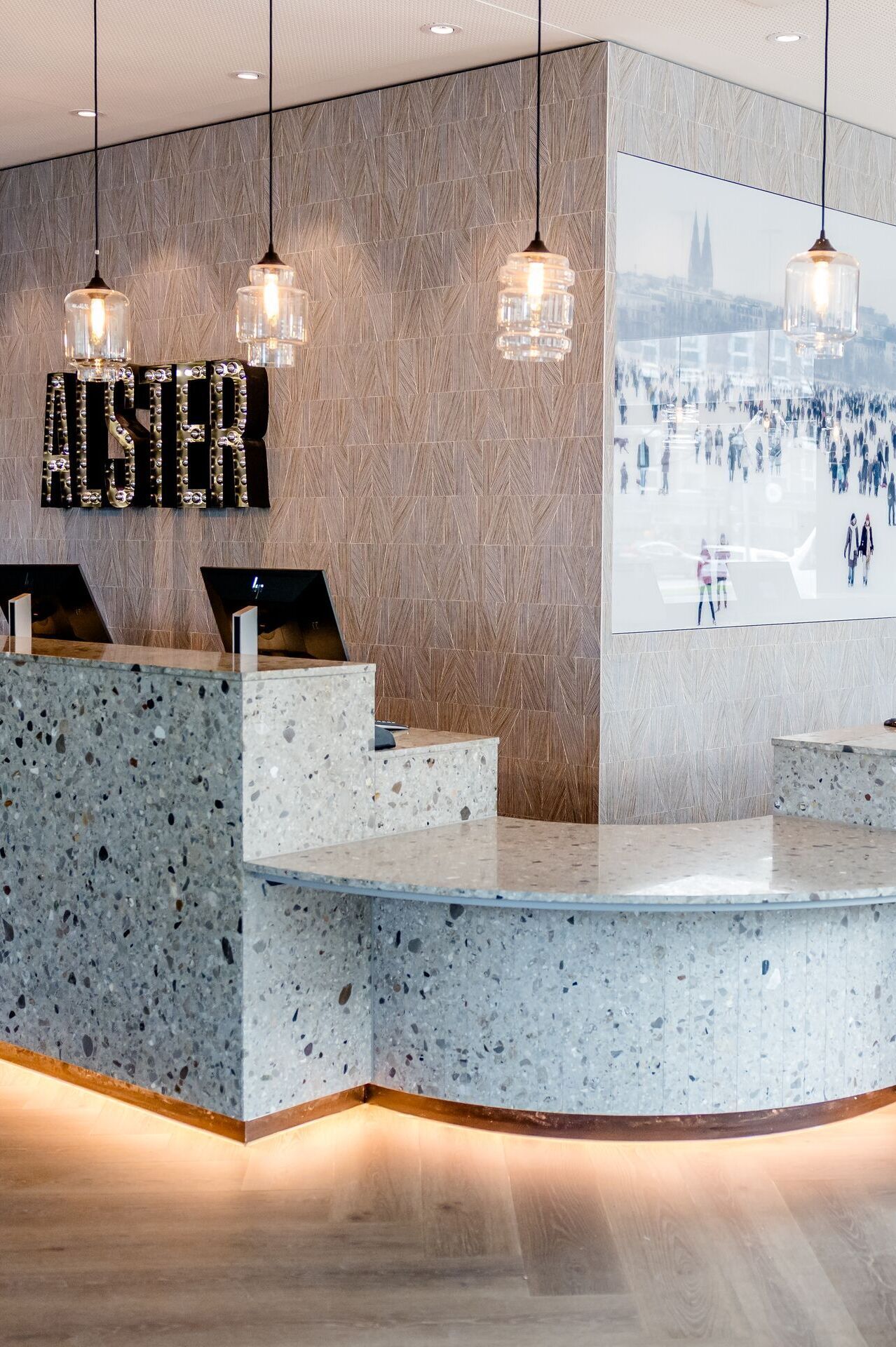 Hotel Hamburg-Alster Motel One Empfangsbereich mit marmoriertem Tresen, mehreren Computern und stilvollen Hängelampen.