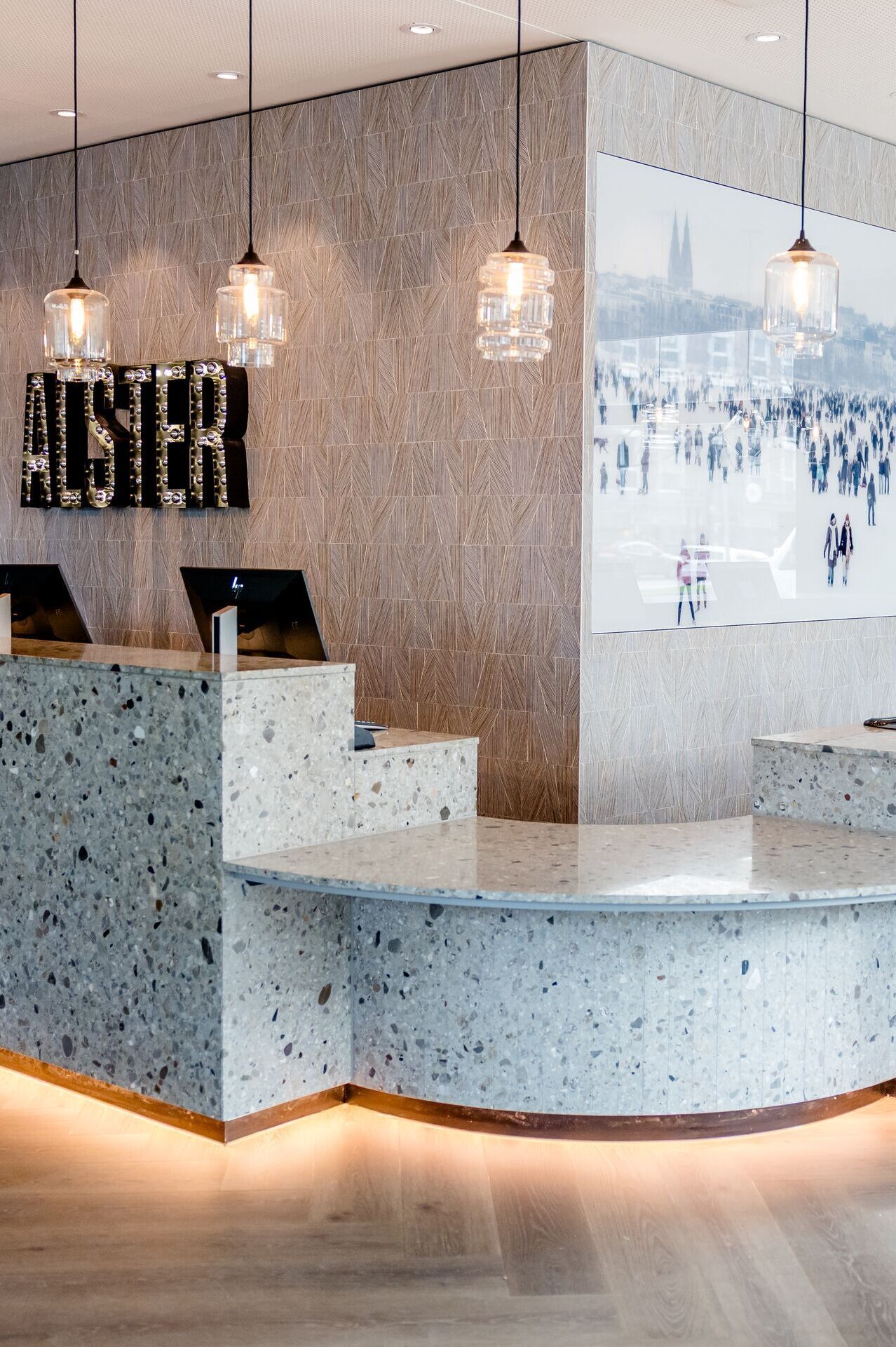 Hotel Hamburg-Alster Motel One Empfangsbereich mit marmoriertem Tresen, mehreren Computern und stilvollen Hängelampen.