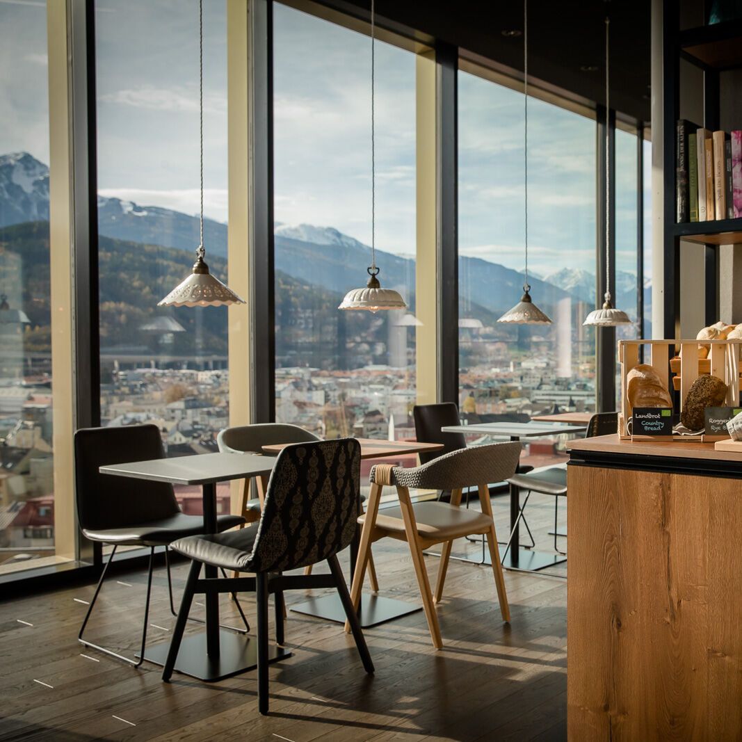 designhotel Innsbruck Motel One breakfast area with several seating areas and floor-to-ceiling windows with views of the mountains and city