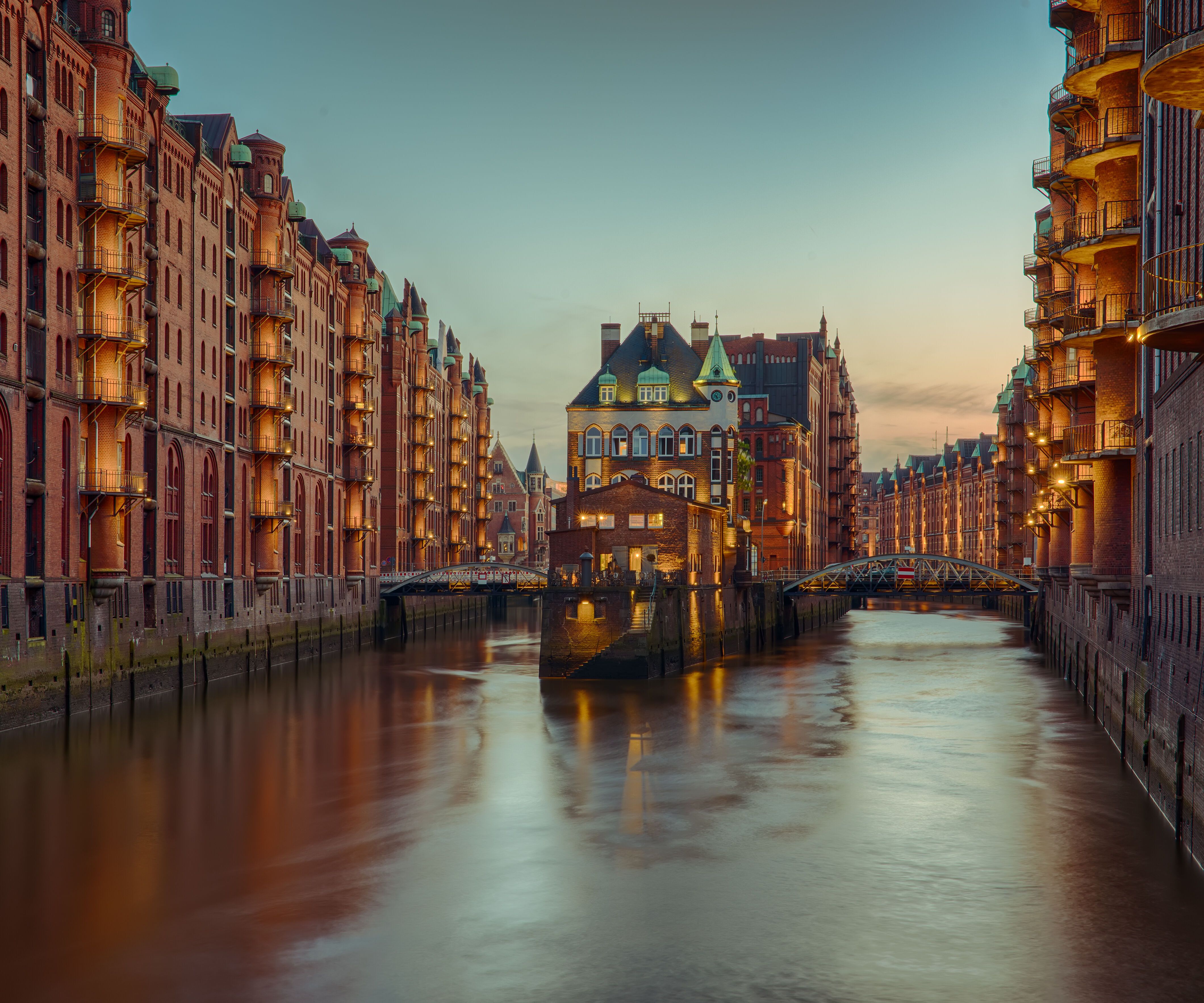 Blick auf einen ruhigen Kanal umgeben von historischen Backsteingebäuden bei Sonnenuntergang, mit warmem Licht, das die Fassaden erhellt und eine einladende, friedliche Atmosphäre schafft.