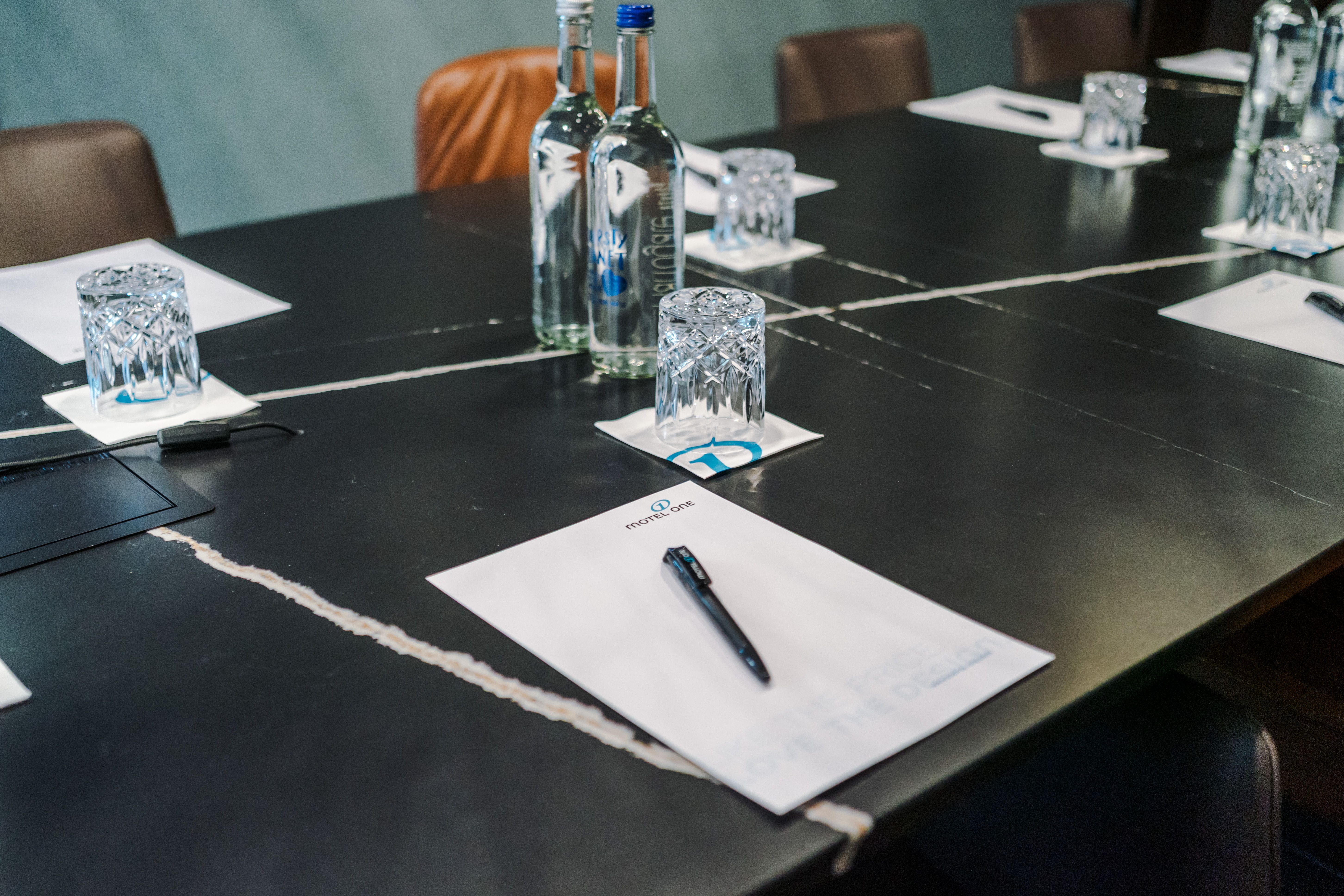 Konferenzraum mit großem Tisch, ausgestattet mit Schreibblöcken, Stiften, Wassergläsern und Wasserflaschen, vorbereitet für ein Meeting oder Seminar.